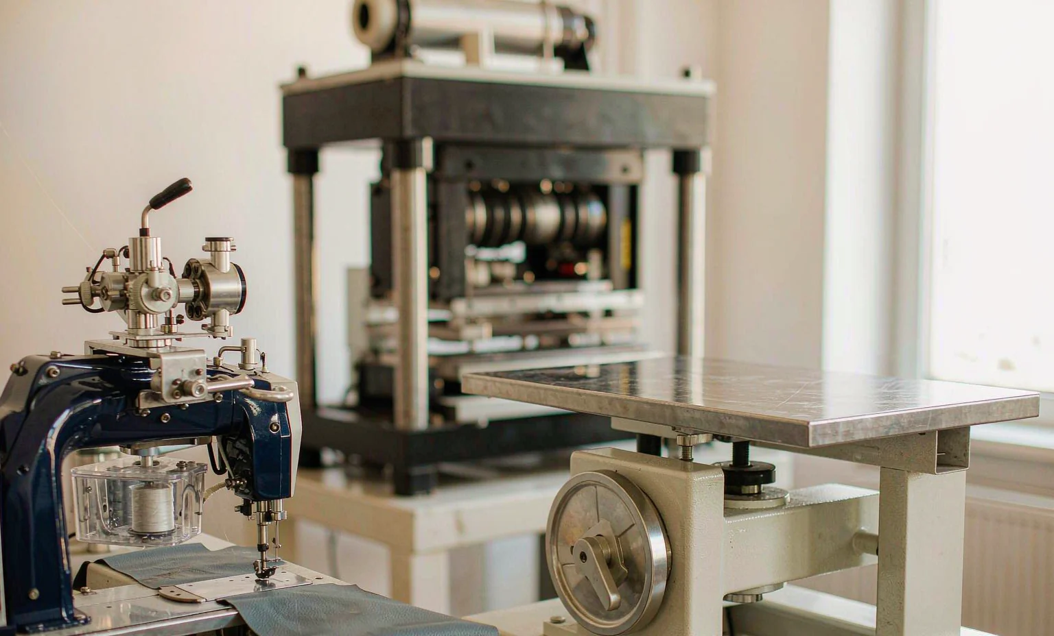 A computerized pattern sewing machine stitching a PU leather panel, with a die-cutting press behind